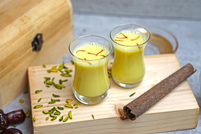 Two glasses of yellow liquid with saffron on a wooden board with spices and dates.