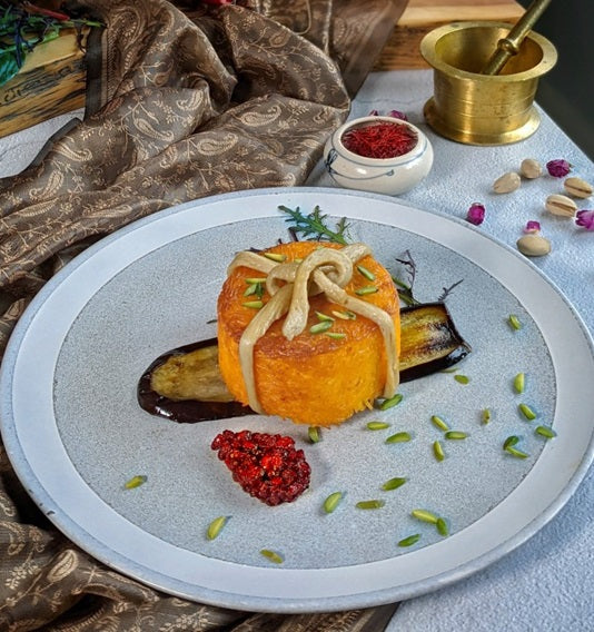 Gourmet dish with roasted sweet potato, eggplant, and garnishes on a textured plate.